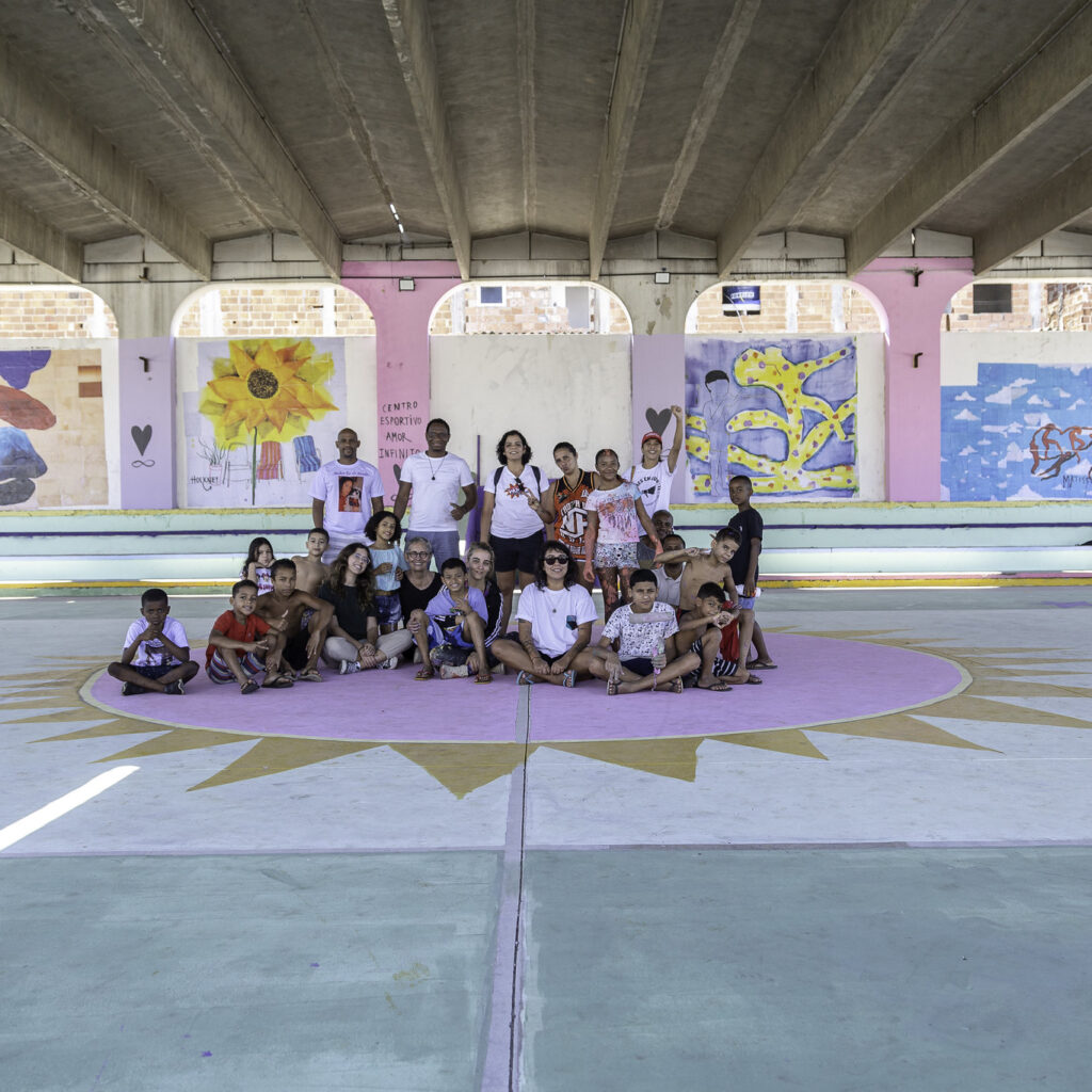 Artistas e crianças reunidos no centro da quadra poliesportiva revitalizada por eles