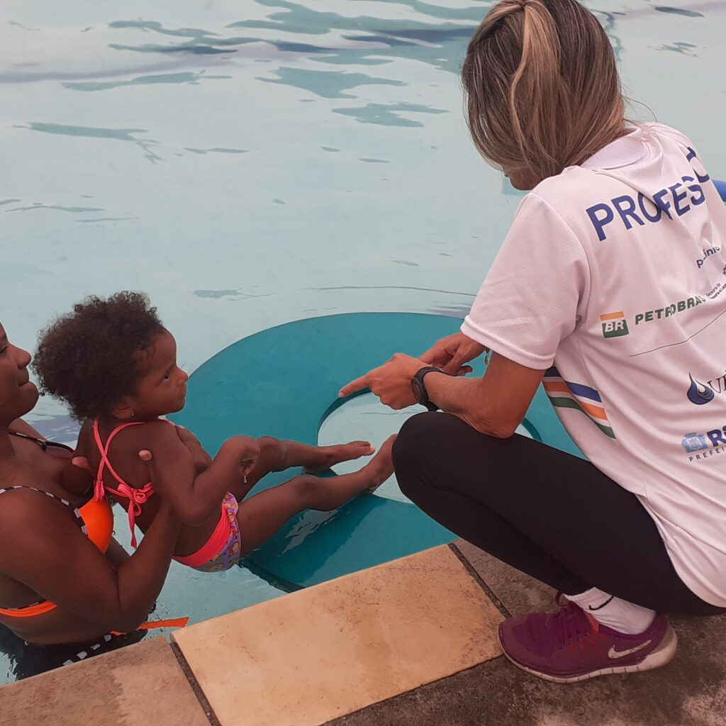 Professora auxilia criança com a mãe em piscina com uma boia